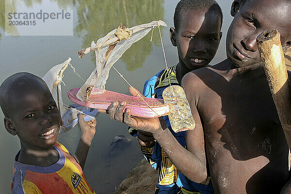 Drei Songhai-Kinder zeigen ein Spielzeugboot aus einer Sandale und einem Sardinendosendeckel am Niger  Mali  Westafrika