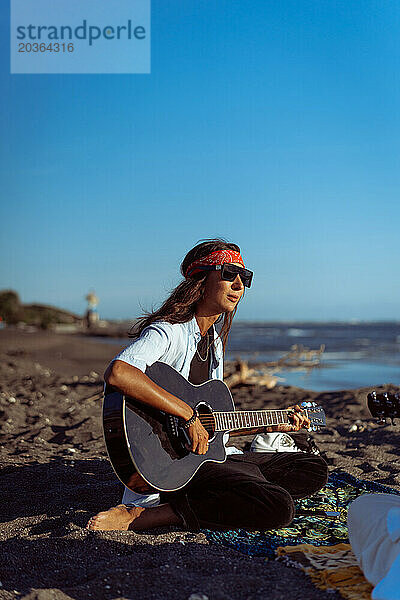 Musikerin singt und spielt Gitarre am Strand. In einem Bandana. Bali