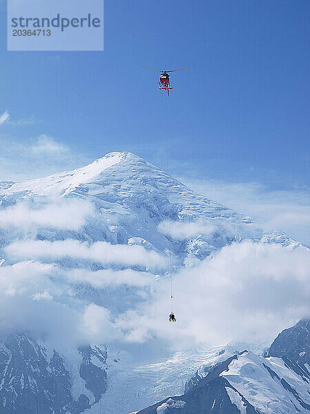 Ein Rettungshubschrauber vom Typ A Star führt eine Langleinen-Rettungsmission auf dem Mount McKinley in Alaska durch. Unter dem Helikopter baumelt ein Bergretter an einem Seil. Halterung für