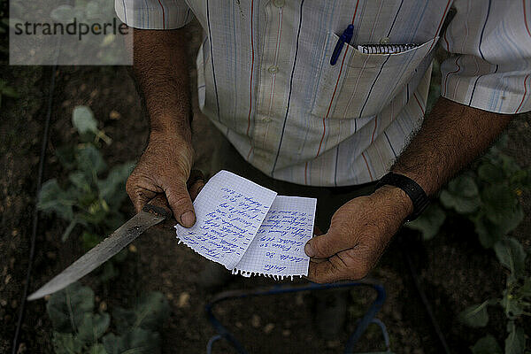 Ein Bauer  der ein Messer in der Hand hält  schaut sich während der Arbeit seine Notizen an