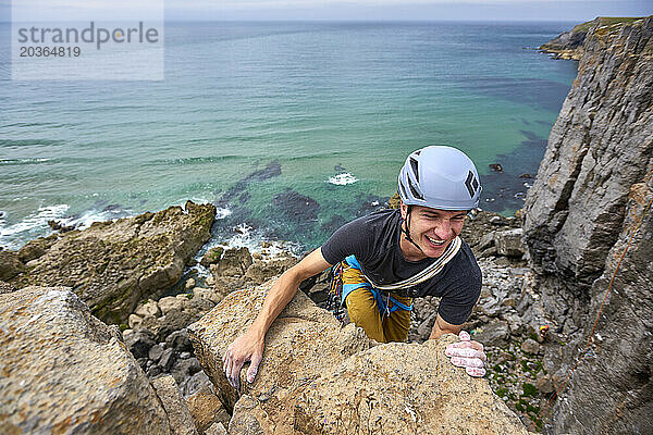 Lächelnder abenteuerlustiger Mann mit Schutzhelm beim Klettern am Meeresufer  Pembroke  Wales  Großbritannien