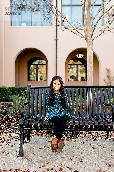 Sechsjähriges Mädchen mit schüchternem Lächeln auf einer Bank in San Diego