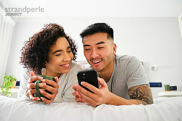Gemischtrassiges glückliches Paar nutzt das Smartphone im Bett.
