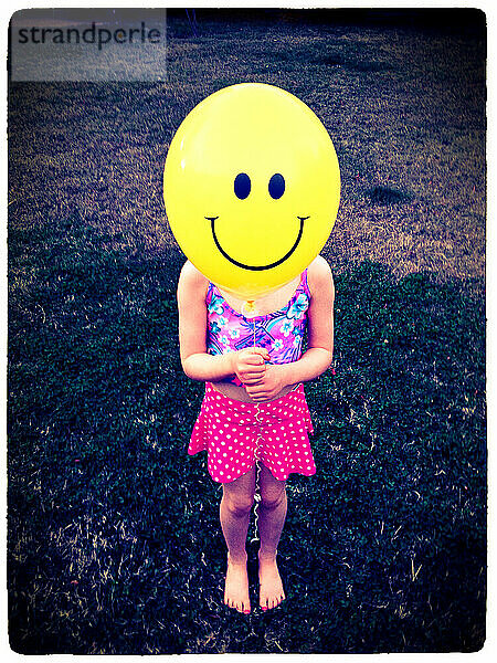 Ein gelber Ballon mit einem Smiley drückt die Freude des jungen Mädchens aus  das ihn an einem Sommerabend hält – Fair Oaks  Kalifornien