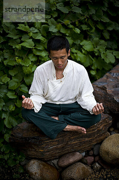 Ein laotischer Mann sitzt zur Meditation in einem Garten.