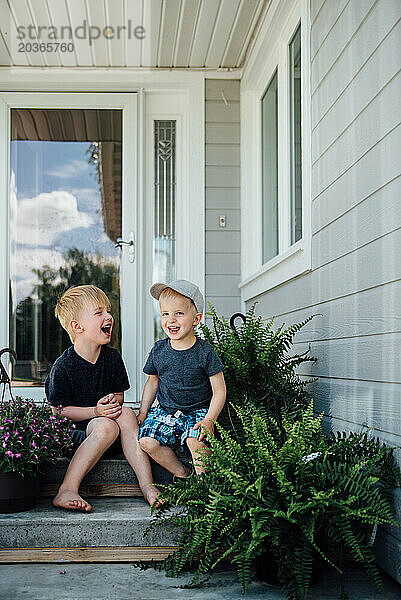 Zwei kleine Jungen lachen sich im Sommer auf der Vordertreppe aus.