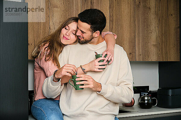 Spanisches junges Paar umarmt sich verliebt  während es in der Küche einen Kaffee trinkt.
