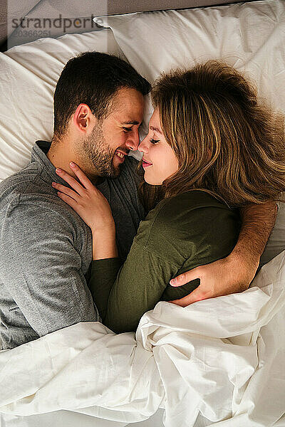 Draufsicht auf ein spanisches Paar  das sich verliebt in einem Bett umarmt.