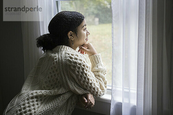 Ein gemischtrassiges Teenager-Mädchen blickt mit friedlicher Miene aus dem Fenster