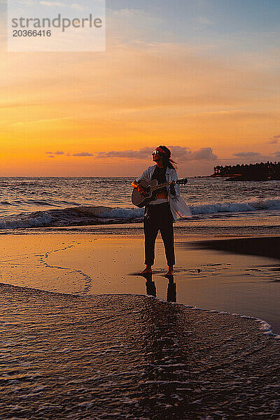 Musikerin mit Gitarre am Strand bei Sonnenuntergang. Bali