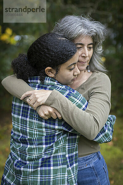 Eine weiße Mutter umarmt und tröstet ihre gemischtrassige Teenager-Tochter
