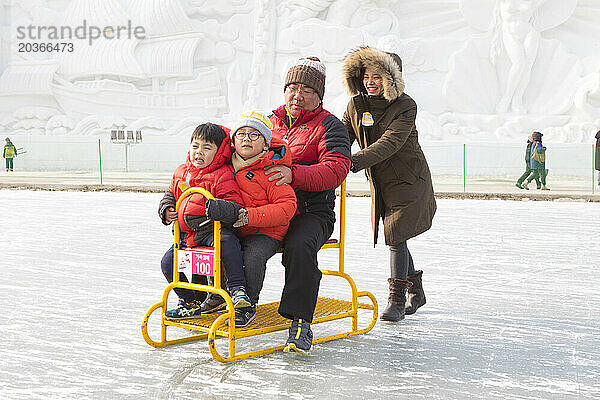 Asiatische Familie vergnügt sich auf Gruppenschlitten auf dem zugefrorenen Fluss  Hwacheon Sancheoneo Ice Festival  Gangwon-do  Südkorea