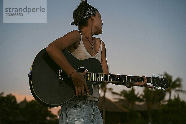 Musikerin singt und spielt Gitarre am Strand. In einem Bandana. Bali