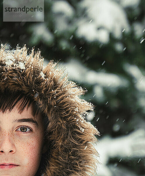 Nahaufnahme eines Jungen mit pelziger Kapuze draußen im Schnee an einem Wintertag.