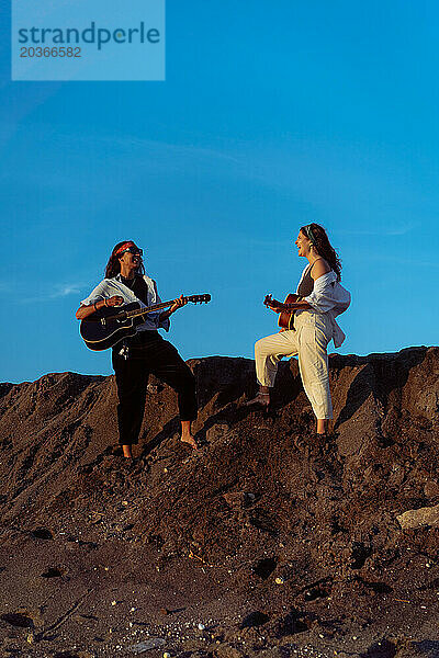 Freundinnen spielen Gitarren am Strand. Sonnenuntergang am Meer. Bali