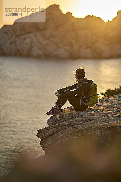Blick auf eine Frau  die auf einer Klippe am Meer sitzt  Sardinien  Italien