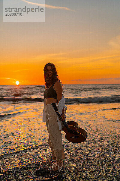 Musikerin mit Gitarre am Strand bei Sonnenuntergang. Bali