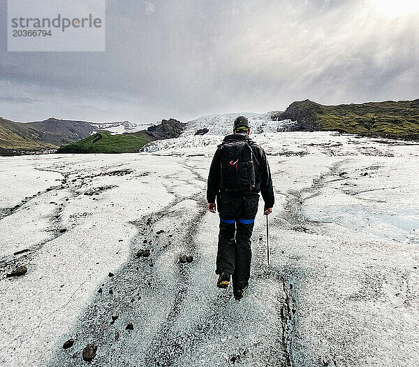 Mann wandert bei strahlendem Sonnenschein und Spikes und Geschirr den Gletscher hinauf