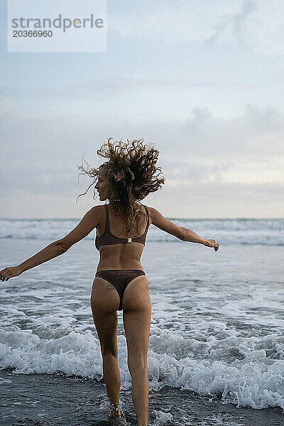 Porträt einer fröhlichen jungen Frau mit glücklichem lockigem Haar am Meer. Bali