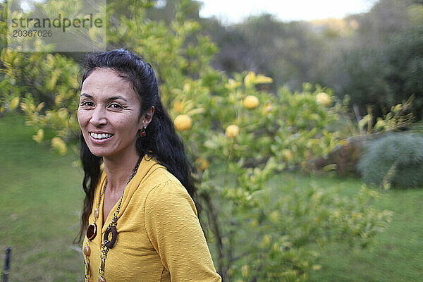 Eine asiatisch-amerikanische Frau steht draußen neben einem Zitronenbaum und blickt lächelnd in die Kamera in Del Mar  Kalifornien.