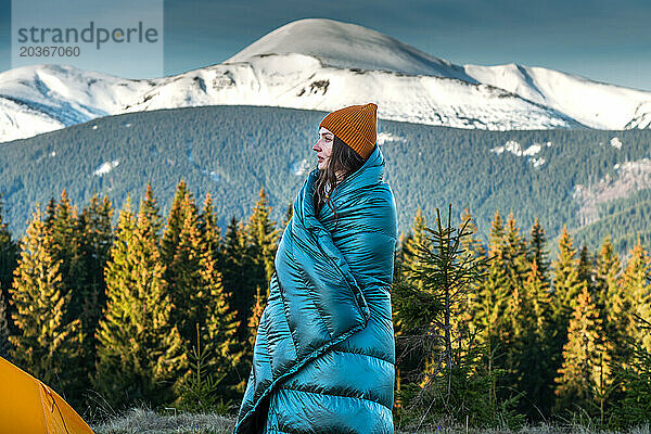 Porträt einer lächelnden Frau  die in eine Decke gewickelt ist  in den verschneiten Bergen