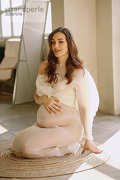 Porträt einer attraktiven schwangeren Frau im elfenbeinfarbenen Kleid