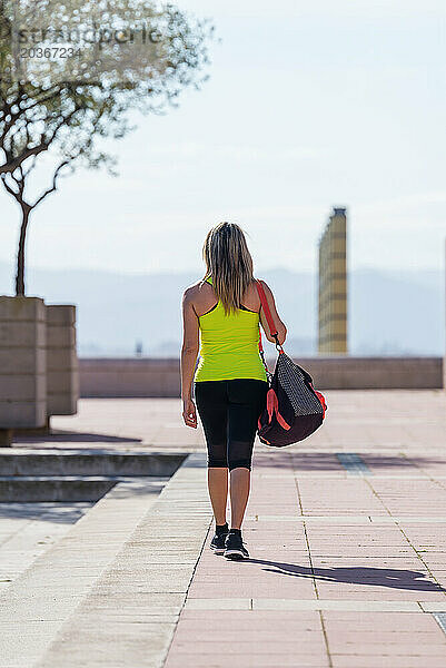 Rückansicht einer mittleren erwachsenen Frau  die mit einer Sporttasche auf den Schultern im Freien spaziert