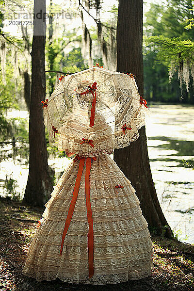 Eine junge Frau posiert in einem Southern Belle-Outfit  einschließlich eines großen  verzierten historischen Kleides und Sonnenschirms  in der Nähe eines Sees.