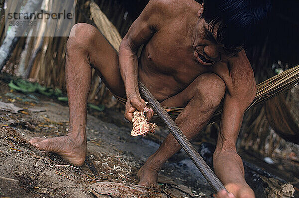 Yanomami-Indianer formt aus dem Kieferknochen eines Pekari einen Jagdbogen. Im Amazonaswald im Süden Venezuelas.