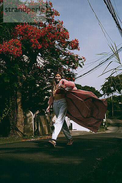 Junge Frau mit langen Haaren im Kimono geht auf Bali die Straße entlang.