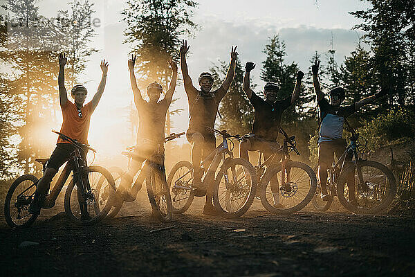 Fröhliche junge Menschen posieren mit ihren E-Bikes bei Sonnenuntergang