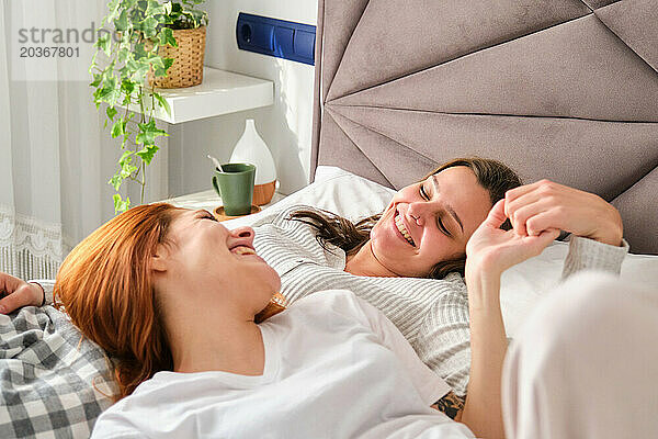 Glückliches romantisches lesbisches Paar  das Händchen haltend zusammen auf dem Bett liegt.