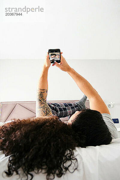 Multiethnisches glückliches Paar  das mit dem Telefon ein Selfie im Bett macht.