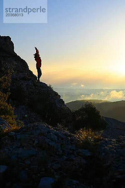 Silhouette einer Frau  die bei Sonnenaufgang ihre Arme hebt.