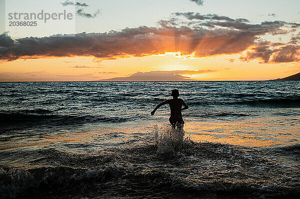 Silhouette eines Kindes  das bei Sonnenuntergang auf Maui im ??Meer läuft