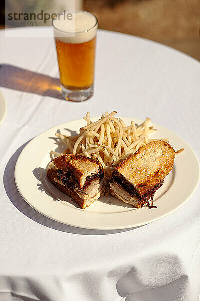 Sandwich-Pommes und ein Bier auf einem Tisch draußen