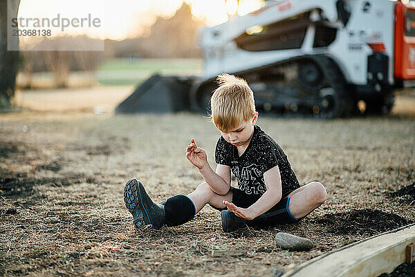 Weite Sicht auf einen kleinen Jungen  der auf dem Boden sitzt und mit Gras spielt