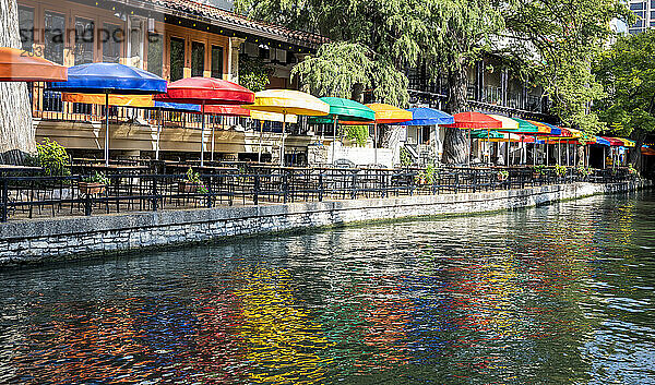 An einem sonnigen Spätsommertag decken bunte Sonnenschirme die Tische in einem Restaurant am San Antonio River Walk ab.