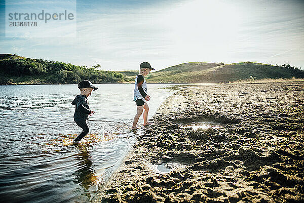 Seitenansicht von zwei kleinen Jungen  die an einem Sommerabend in einem See spielen.