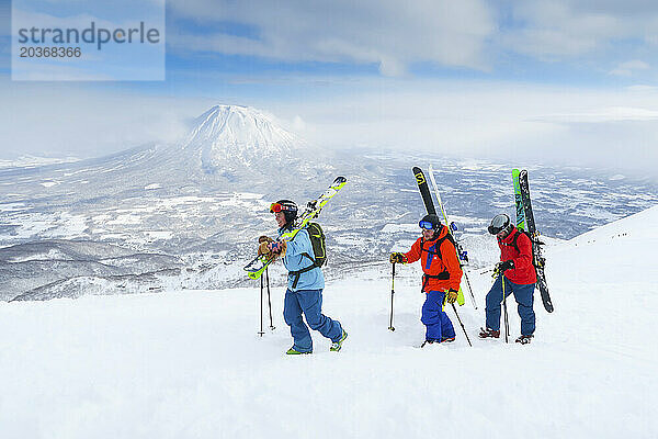 Mit dem Vulkan Yotei im Hintergrund wandern eine Frau und zwei männliche Backcountry-Skifahrer zum Gipfel des Mount Annupuri im Skigebiet Niseko United auf der japanischen Insel