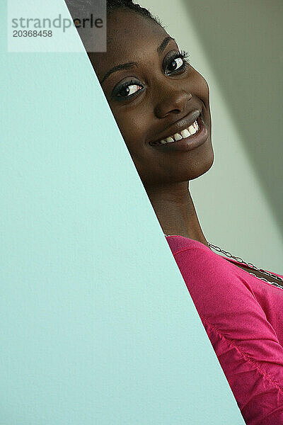 Porträt einer jungen schwarzen Studentin  die auf dem Campus an einer Wand lehnt.