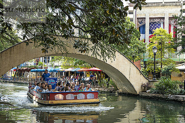 An einem sonnigen Spätsommertag fährt eine Menschenmenge in einem Wassertaxi den San Antonio River entlang.