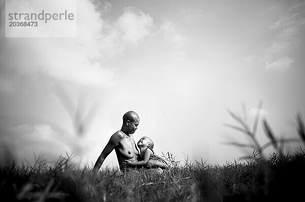 Sohn sitzt auf dem Schoß der Mutter in der Sonne  am Red River  Vietnam.