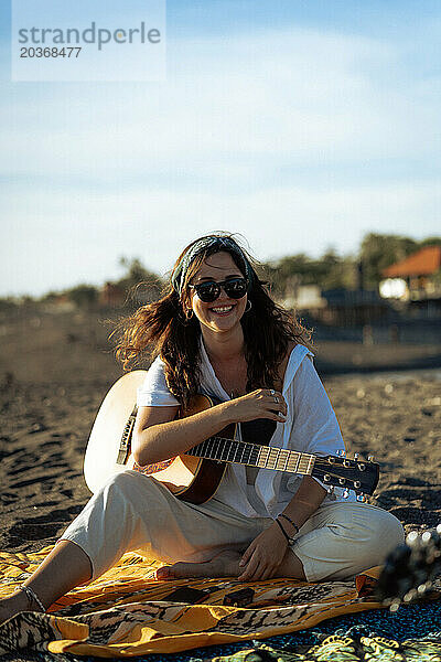 Musikerin singt und spielt Gitarre am Strand. In einem Bandana. Bali