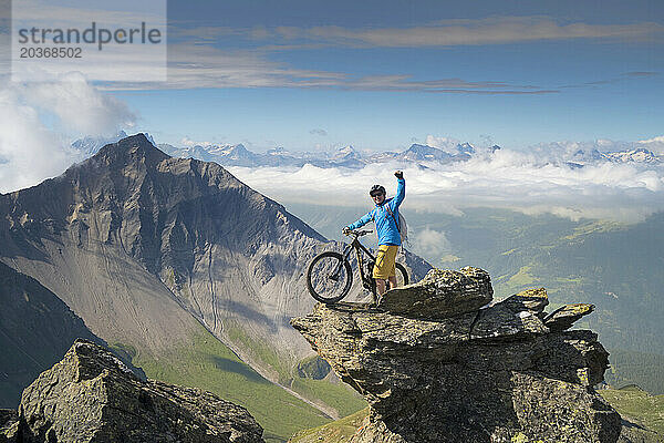 Ein Mountainbiker steht auf einem felsigen Gipfel in der Nähe des Weisshorns  einem Alpengipfel. Die Region Lenzerheide in Graubünden in der Schweiz ist ein Singletrail-Paradies.
