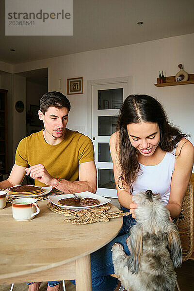 Frau streichelt ihren Hund  während sie mit ihrem Freund frühstückt.