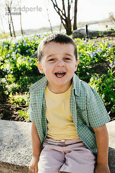 Kleiner Junge lächelt glücklich im Sonnenschein  mit Frühlingsblumen dahinter