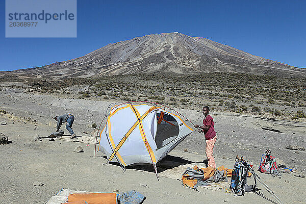 Zwei tansanische Träger bauen an den Hängen des Kilimandscharo ein Zelt für ihre westlichen Kunden auf.