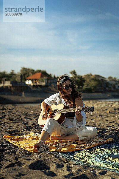 Musikerin singt und spielt Gitarre am Strand. In einem Bandana. Bali