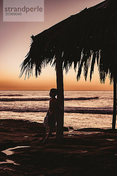 Silhouette eines Jungen mit dem Meer und Sonnenuntergang im Hintergrund